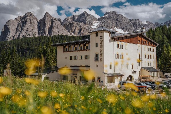 A hotel with a mountain backdrop, featuring a prominent entrance and a parking area. - B&B Hotel Passo Tre Croci Cortina (Cortina d'Ampezzo)
