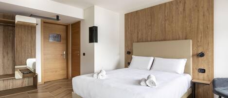 Ein modernes Hotelzimmer mit einem großen Bett, Holzvertäfelung an den Wänden, einer integrierten Garderobe und einer kleinen Sitzecke.