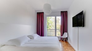 A modern bedroom with a large bed, a TV mounted on the wall, and a window with curtains. - Fauriel Aimé - Prestations haut de gamme - St Etienne (Saint Etienne)
