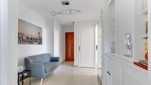 A hallway with a grey sofa, white cabinets, and a door leading to another room. - Fauriel Aimé - Prestations haut de gamme - St Etienne (Saint Etienne)