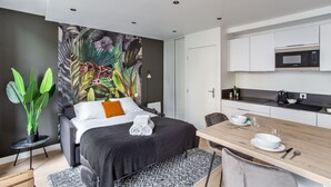 A modern hotel room with a bed, a dining table, a microwave, and a large tropical mural on the wall. - Le Kipling - Studio de Standing à 5 min du centre (Rennes)