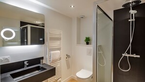 A modern bathroom with a glass-enclosed shower, a white toilet, a black sink with a mirror, and a towel rack. - Le Kipling - Studio de Standing à 5 min du centre (Rennes)