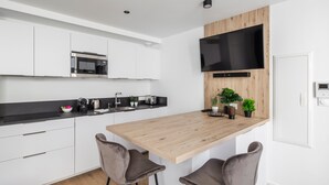 A modern kitchen with white cabinets, a wooden island, two bar stools, a flat-screen TV, and a coffee machine. - Le Kipling - Studio de Standing à 5 min du centre (Rennes)