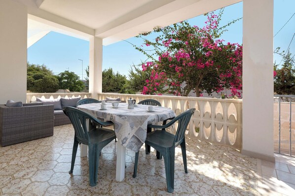 A covered outdoor dining area with a table set for two, surrounded by chairs, and a sofa.