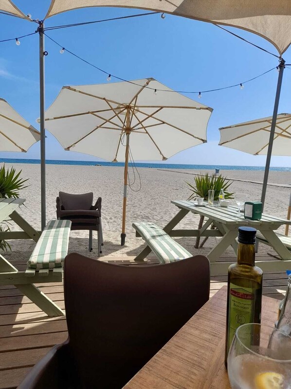 Une terrasse au bord de la plage, avec des sièges extérieurs, des parasols et une vue sur l’océan.