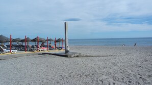 Een strand met ligbedden en parasols, een redershut en de oceaan op de achtergrond.