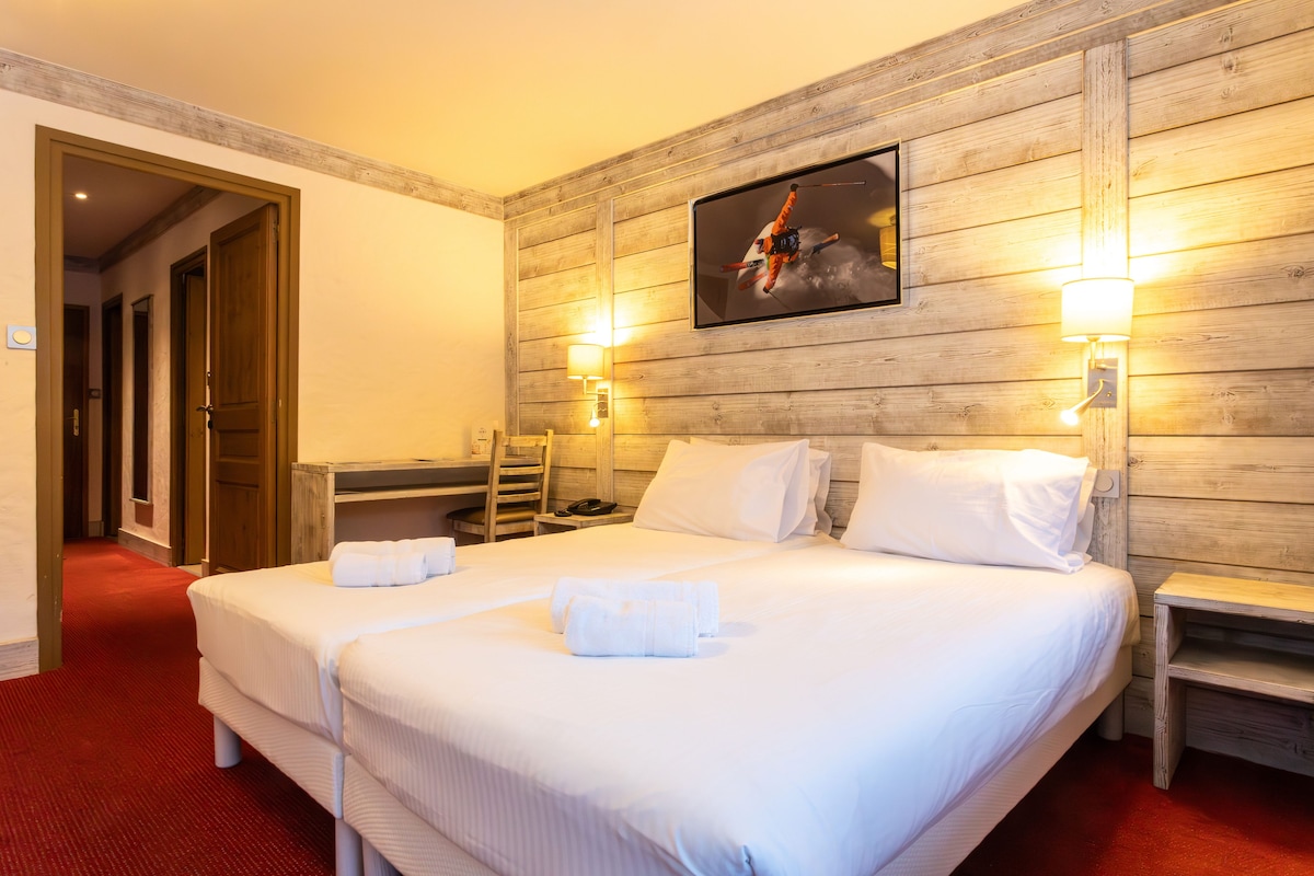 Habitació d'hotel amb un llit gran, panell de capçalera de fusta, dues làmpades de nit i una obra d'art amb temàtica d'esquí a la paret.