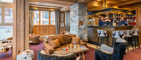 A cozy lounge area with wooden furniture, a stone pillar, and a bar with various bottles.