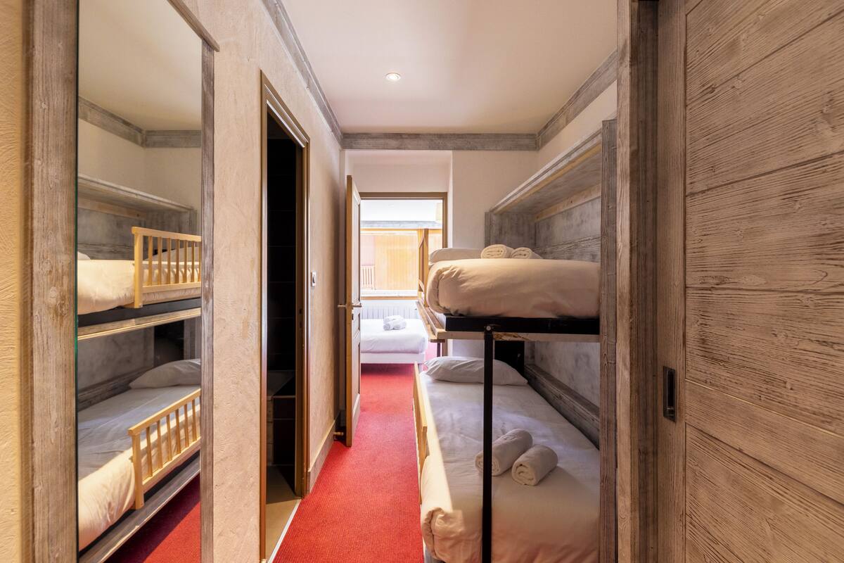 A hotel room with bunk beds, a wooden wall, and a red carpet.