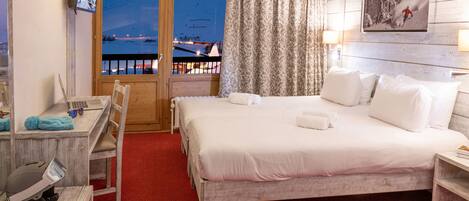 Habitación de hotel con cama, escritorio, silla, televisor y balcón con vista a un paisaje nevado.