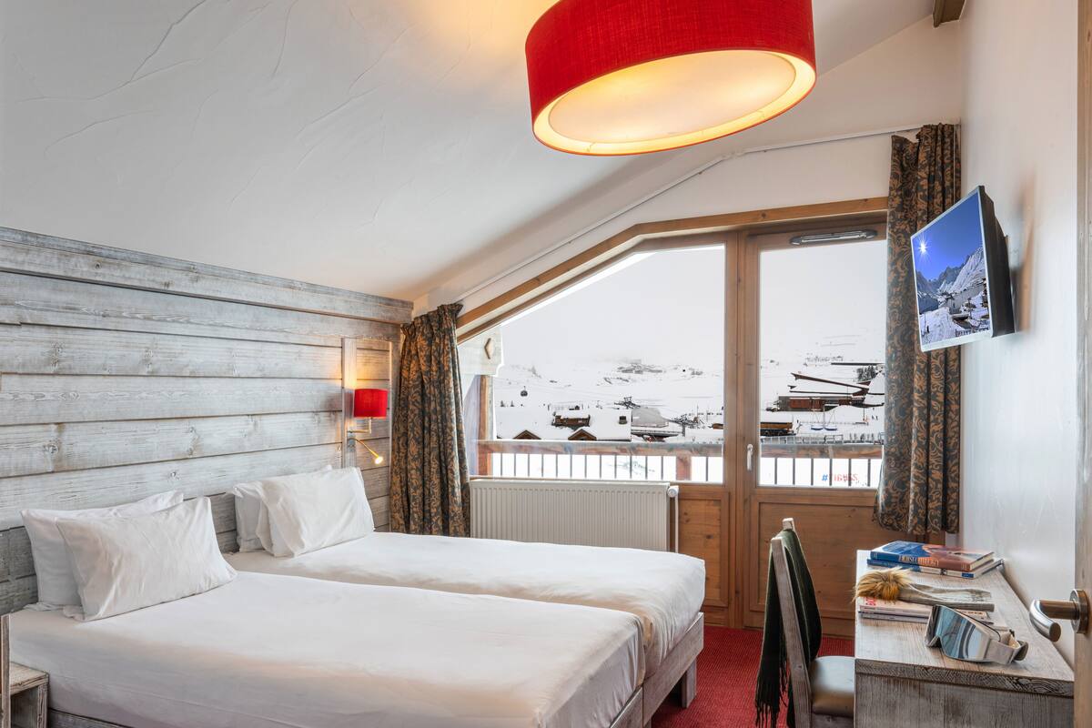 A hotel room with two beds, a desk, a TV, and a window with a view of a snowy landscape.