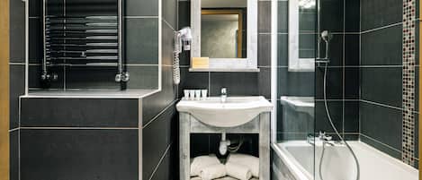 Un baño moderno con pared de azulejos negros, un lavabo blanco, un espejo y una bañera.