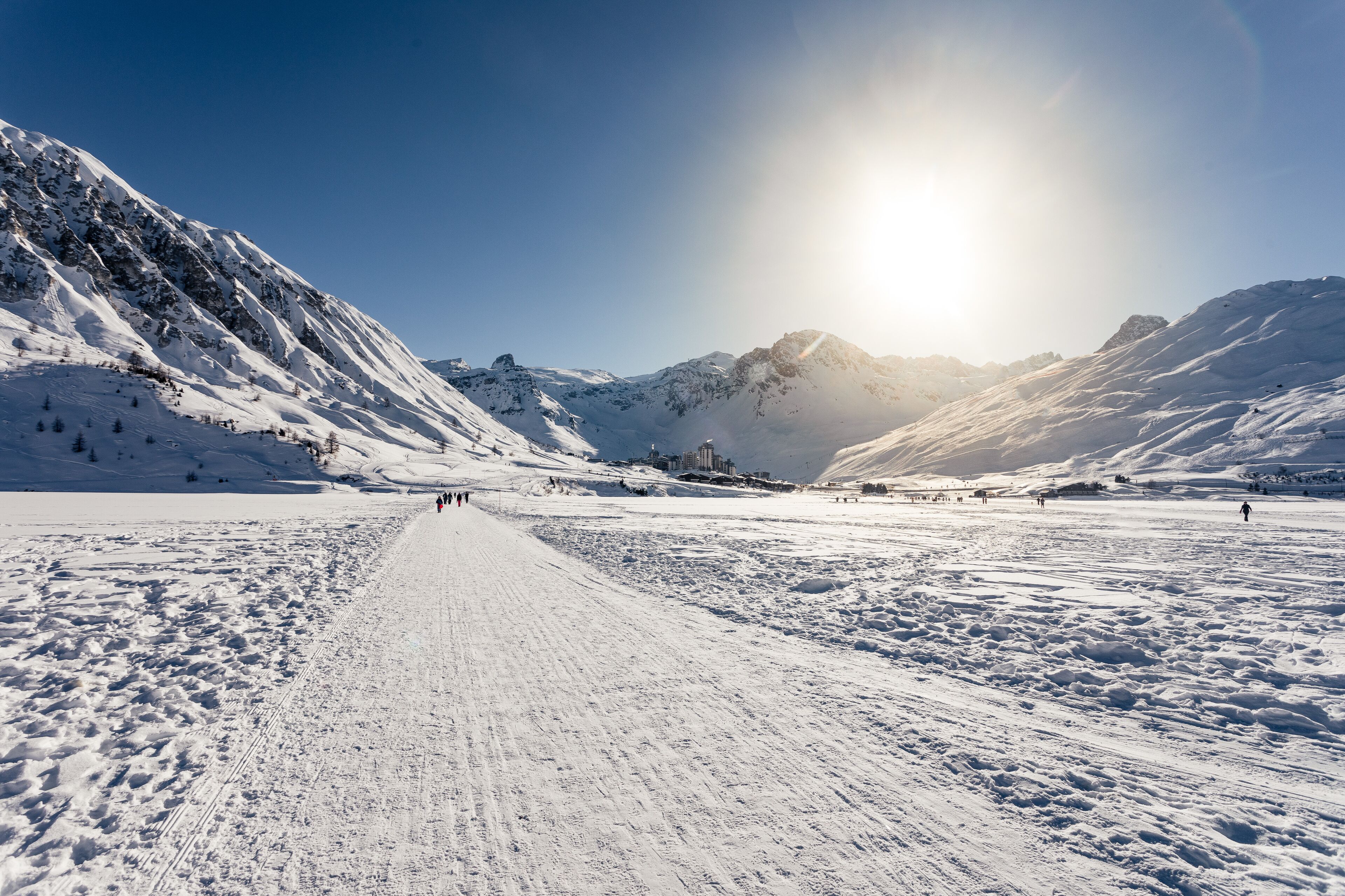 A snow-covered mountain path with a clear sky and distant buildings.