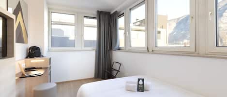 A hotel room with a bed, a desk with a laptop, a chair, and a window with curtains.
