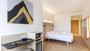 Una habitación de hotel moderna con una cama, un escritorio con computadora, una silla y un mueble pequeño.