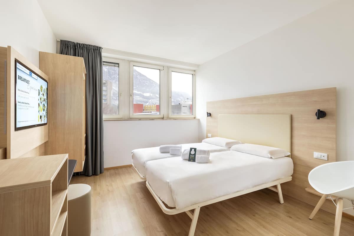 Une chambre d’hôtel moderne équipée d’un lit, d’un bureau et d’un téléviseur qui affiche les options proposées pour le petit-déjeuner.