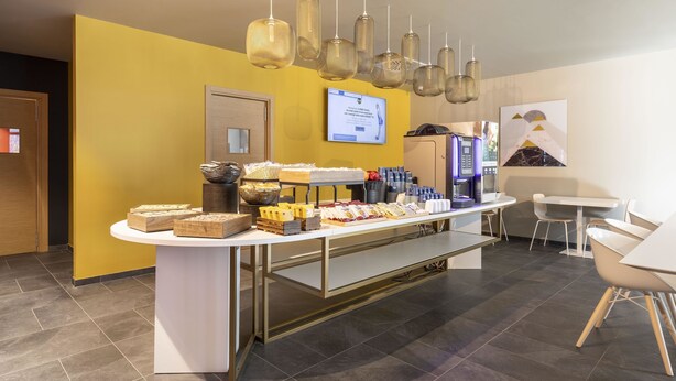 A breakfast buffet area with a variety of food items, a digital screen, and modern lighting fixtures.