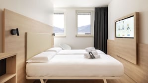 A hotel room with two beds, a TV mounted on the wall, and a view of mountains through the windows.