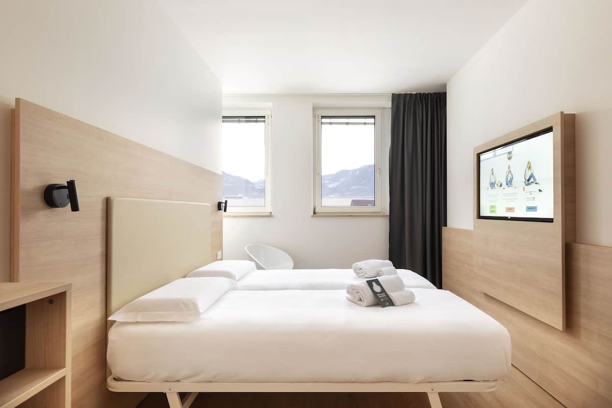 Une chambre d’hôtel avec deux lits, un téléviseur fixé au mur et une vue sur les montagnes par les fenêtres.