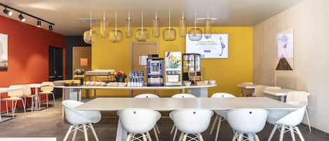 Une salle de conférence moderne, dotée d’une longue table et de chaises blanches, d’un coin café et d’un mur d’accent jaune.