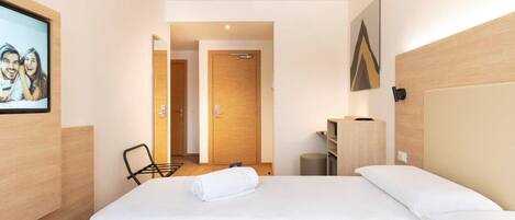 A hotel room with a large bed, a desk, a chair, and a door leading to another room.