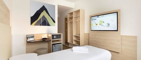 Habitación de hotel con cama, escritorio con ordenador, televisor mostrando una aplicación de compras y armario.