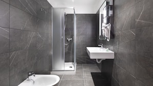 A modern bathroom with a glass-enclosed shower, a pedestal sink, and a vanity mirror.