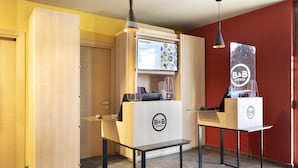 A hotel reception area with a wooden counter, a digital menu board, and a B&B logo.