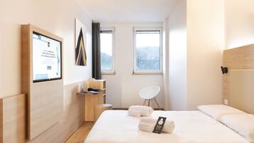 Una habitación de hotel moderna con una cama, un escritorio, una silla y una ventana con vistas a las montañas.