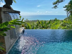 Une piscine à débordement avec une cascade, entourée d’une végétation luxuriante et offrant une vue sur l’océan.