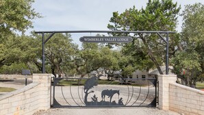 Een metalen hek met een bord waarop 'Wimberley Valley Lodge' staat, en een silhouet van een cowboytafereel.