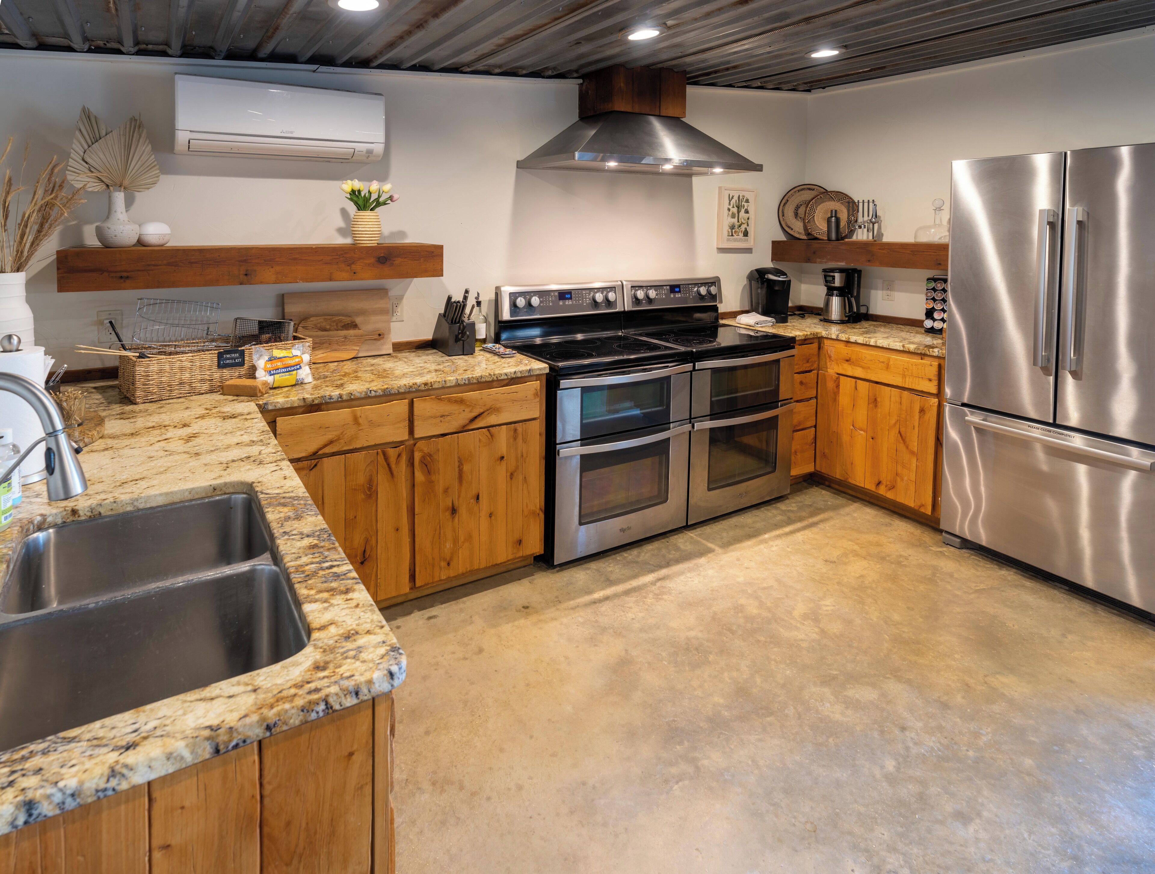 Una cocina con armarios de madera, un refrigerador de acero inoxidable, un horno doble y una encimera de granito.