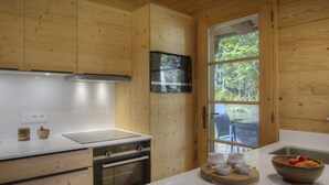 A modern kitchen with wooden cabinetry, a stainless steel refrigerator, a built-in oven, and a large window providing a view of the outdoors. - Chalet Cosyneige for 11 in La Clusaz, hot tub - OVO Network (La Clusaz)
