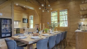 A wooden cabin interior with a dining table set for six, chairs, a kitchen area, and a refrigerator. - Chalet Cosyneige for 11 in La Clusaz, hot tub - OVO Network (La Clusaz)