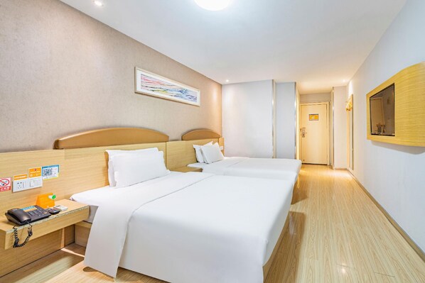 A hotel room with two beds, a desk with a phone and a small table, and a mirror on the wall.