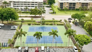 A tennis court surrounded by parking spaces and palm trees, with buildings in the background. - Sea Winds 705: Completely Renovated Beach Front Condo! (Marco Island)