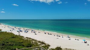 A beach with a wooden walkway leading to the shore, clear turquoise water, and people relaxing on the sand. - Sea Winds 705: Completely Renovated Beach Front Condo! (Marco Island)