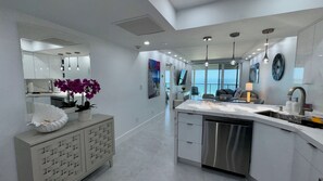 A modern kitchen with a central island, stainless steel appliances, and a view to the outside. - Sea Winds 705: Completely Renovated Beach Front Condo! (Marco Island)
