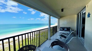A balcony with a view of the beach and ocean, a seating area with chairs and a table, and a wall with a decorative anchor. - Sea Winds 705: Completely Renovated Beach Front Condo! (Marco Island)