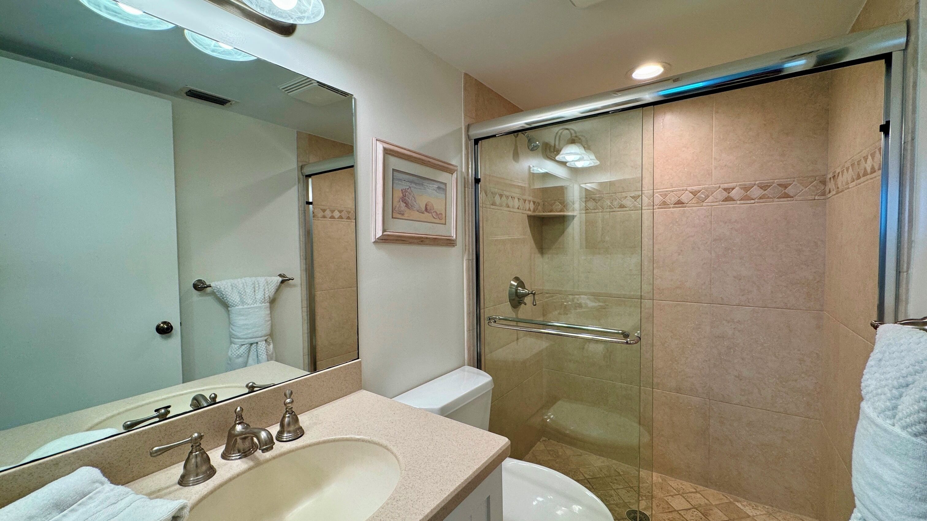 A bathroom with a sink, mirror, toilet, and a glass-enclosed shower.