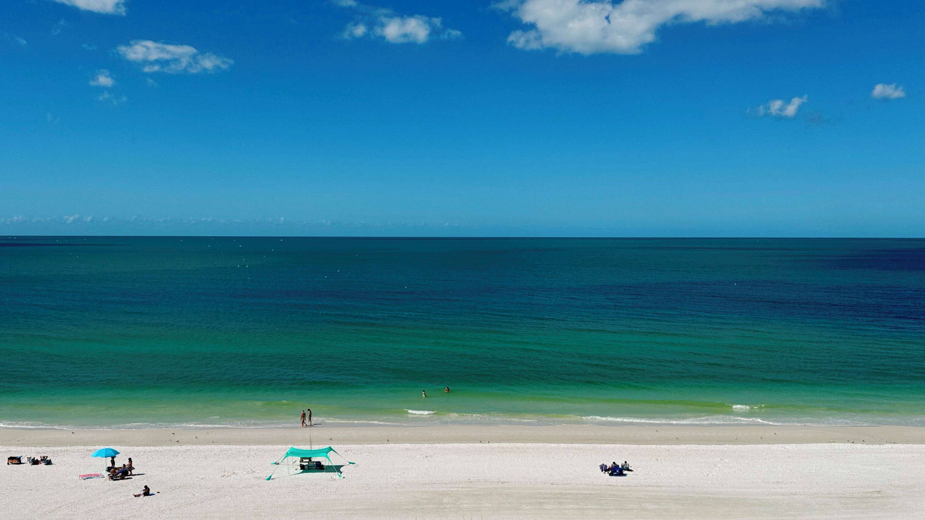A beach with clear turquoise water, a sandy shore, and a few umbrellas and beach chairs.