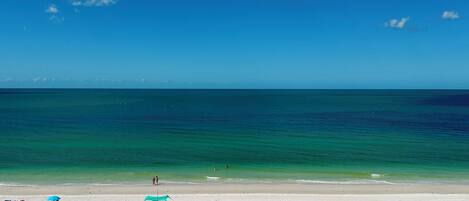 A beach with clear turquoise water, a sandy shore, and a few umbrellas and beach chairs.