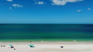 A beach with clear turquoise water, a sandy shore, and a few umbrellas and beach chairs. - Sea Winds 705: Completely Renovated Beach Front Condo! (Marco Island)