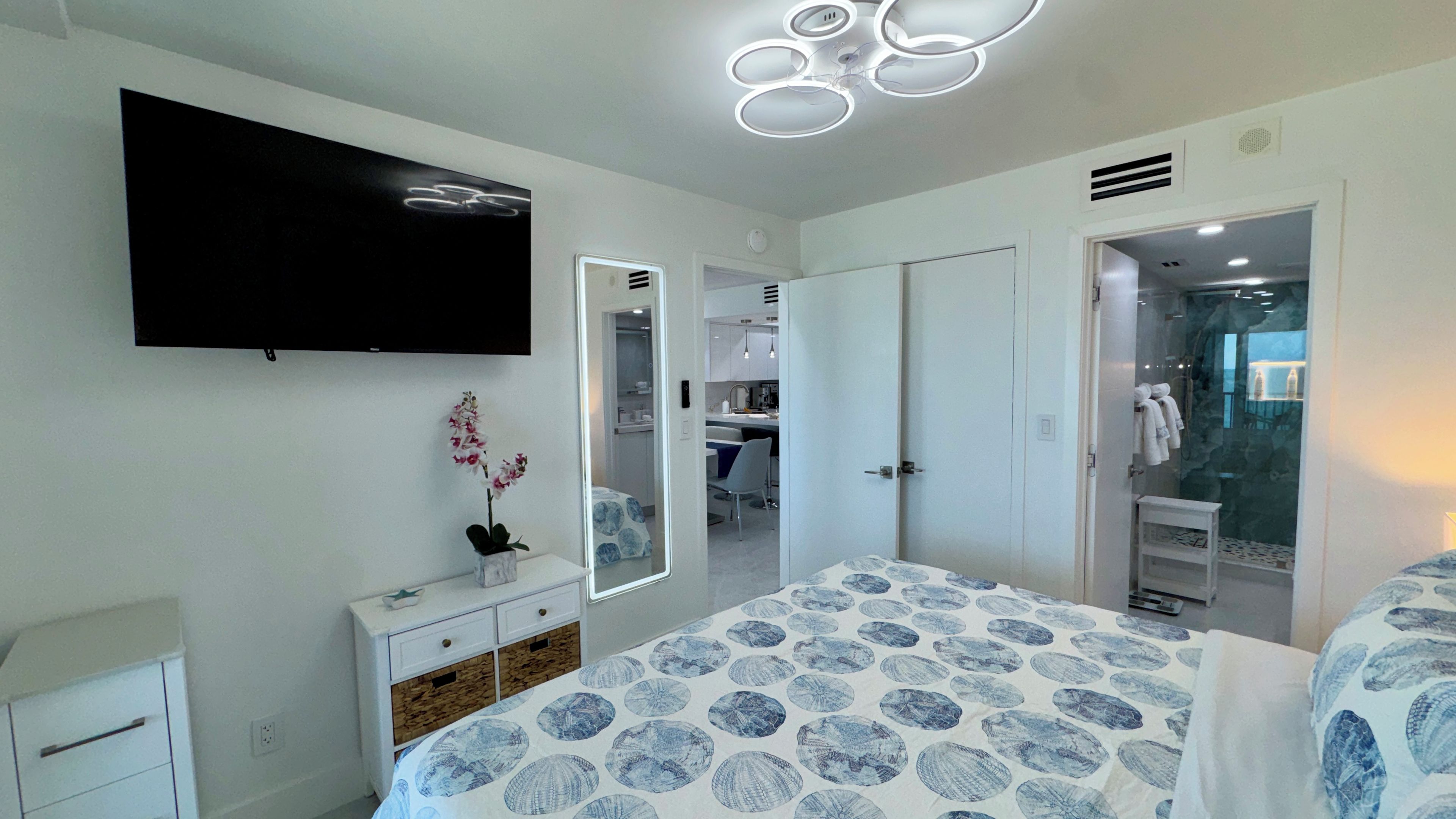 A bedroom with a bed, a dresser, a mirror, a television, and a bathroom visible through an open door.