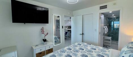 A bedroom with a bed, a dresser, a mirror, a television, and a bathroom visible through an open door.
