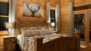 Ett sovrum i en stuga med träpanel, inrett med en säng, sängbord, en tavla som föreställer ett rådjur och en skjutdörr av glas.