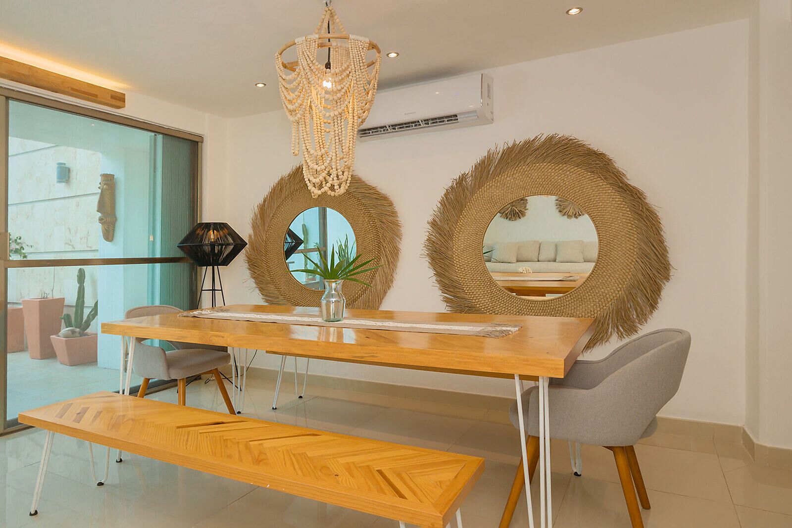 A modern dining area with a wooden table, bench, and two round mirrors with woven frames.