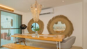 A modern dining area with a wooden table, bench, and two round mirrors with woven frames. - Amazing Beachfront Villa (San Miguel de Cozumel)