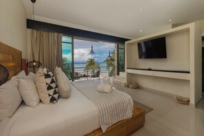 A modern bedroom with a large bed, a TV, and a balcony with a view of the sea. - Amazing Beachfront Villa (San Miguel de Cozumel)