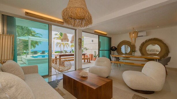 A modern living room with a wooden coffee table, white sofas, and a view of a pool and palm trees. - Amazing Beachfront Villa (San Miguel de Cozumel)